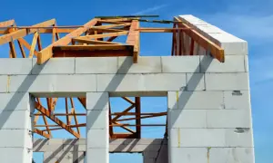 Budowa domu z bloczków silikatowych, widoczna drewniana konstrukcja dachu i niebieskie niebo.