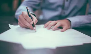 Dłoń pisze długopisem na dokumencie. Może to być ważna scheda spadkowa, która wymaga starannego wypełnienia.
