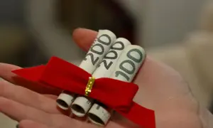 Zrolowane banknoty 100 i 200 zł, przewiązane czerwoną wstążką, leżą na dłoni. To miła darowizna od brata.