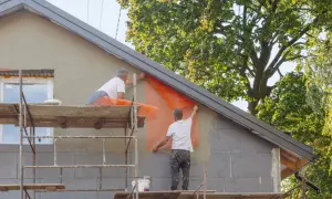 Pracownicy na rusztowaniach montują siatkę elewacyjną, kluczowy etap termomodernizacji budynku.