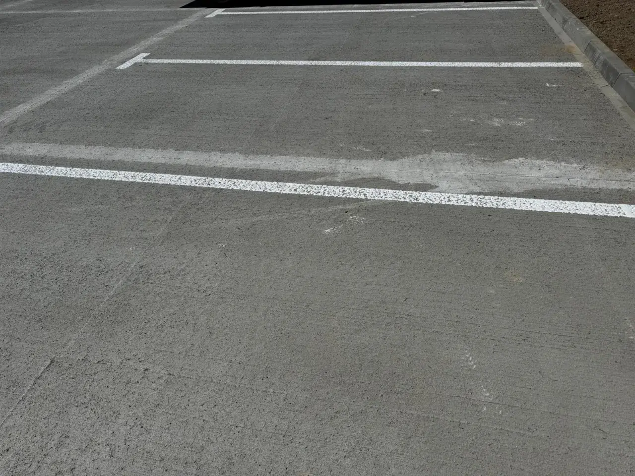 Nowe miejsca parkingowe z białymi liniami wyznaczającymi. Różne rodzaje betonu tworzą trwałą nawierzchnię.