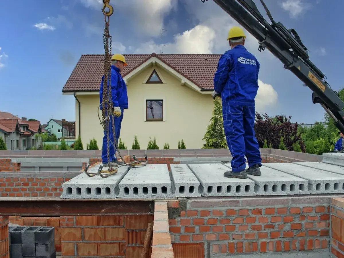 Pracownicy montują prefabrykowane płyty, które są jednym z rodzajów stropów. Budowa domu postępuje.