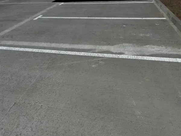 Nowe miejsca parkingowe z białymi liniami wyznaczającymi. Różne rodzaje betonu tworzą trwałą nawierzchnię.